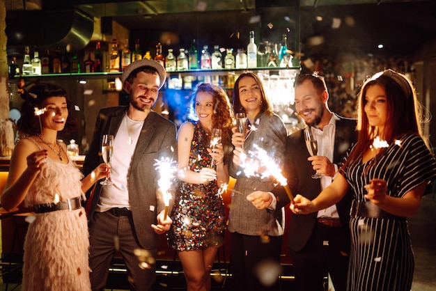 Gruppe glücklicher Menschen, die Wunderkerzen auf der Party halten. Junge Freunde, die mit Champagner anstoßen.