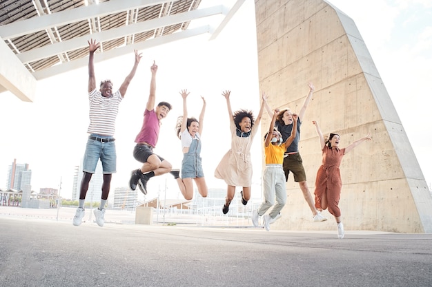 Gruppe glücklicher multiethnischer Freunde, die Spaß haben, junge Studenten außerhalb der Universität springen