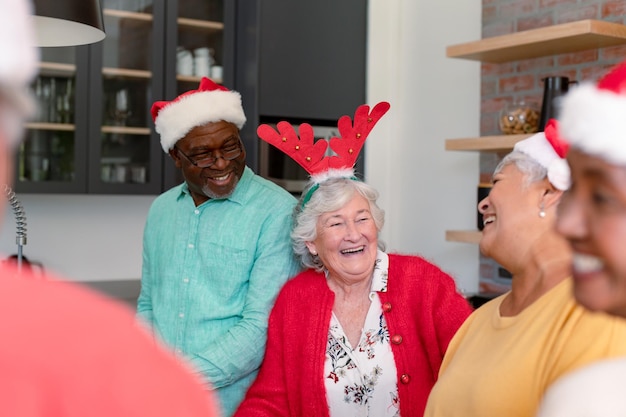 Gruppe glücklicher, vielfältiger älterer männlicher und weiblicher Freunde mit Weihnachtsmützen, die gemeinsam in der Küche kochen