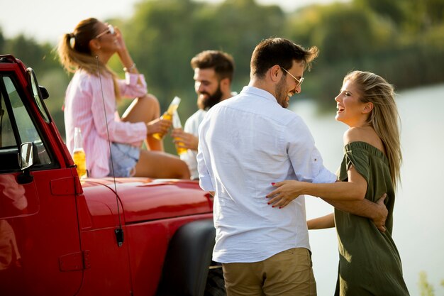 Gruppe junge Leute, die den Spaß mit dem Auto im Freien am heißen Sommertag trinken und haben