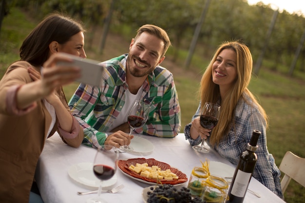 Gruppe junge Leute, die durch die Tabelle sitzen und Rotwein im Weinberg trinken