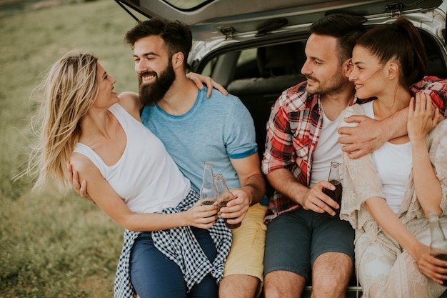 Gruppe junge Leute, die im Auto trank während der Reise in der Natur sitzen