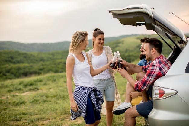 Gruppe junge Leute, die im Auto trank während der Reise in der Natur sitzen