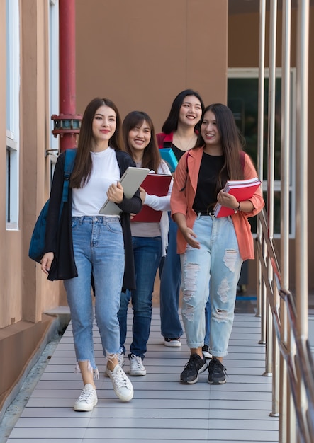 Gruppe junger attraktiver asiatischer Mädchen, die zusammen auf dem Universitätscampus spazieren gehen und vor Freude lächeln. Konzept für Bildung und Studentenleben.