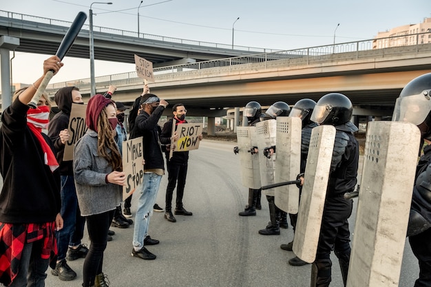 Gruppe junger Demonstranten maskiert mit Schildern und steht vor Polizeiwachen mit Schilden