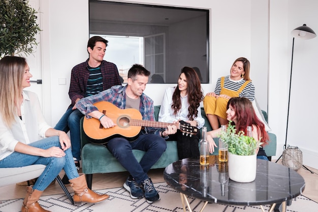 Gruppe junger Freunde, die im Wohnzimmer sitzen, Bier trinken und Gitarre spielen Konzept Lifestyle Spaß Freundschaft
