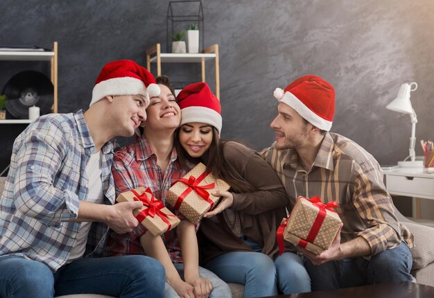 Gruppe junger Freunde, die Weihnachten feiern und zu Hause Geschenke teilen