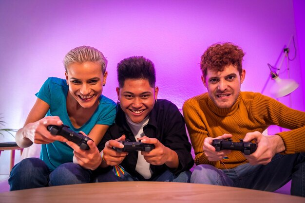 Gruppe junger Freunde, die zusammen Videospiele auf dem Sofa zu Hause spielen, lila geführte junge Millennials