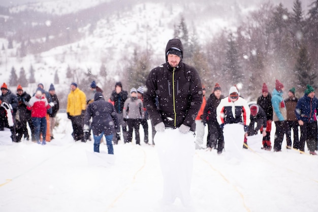 Gruppe junger, glücklicher Geschäftsleute, die bei einem Teambuilding im Bergwald einen Lauf im Taschenwettbewerb haben, während sie den verschneiten Wintertag mit Schneeflocken um sich herum genießen