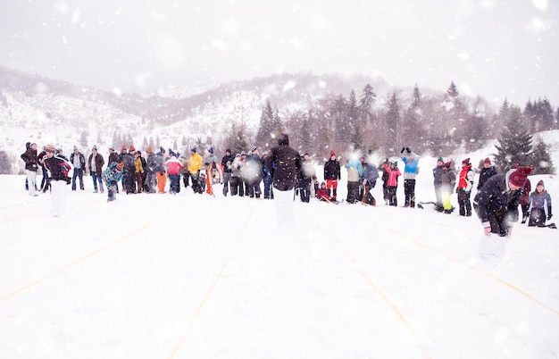 Gruppe junger, glücklicher Geschäftsleute, die bei einem Teambuilding im Bergwald einen Lauf im Taschenwettbewerb haben, während sie den verschneiten Wintertag mit Schneeflocken um sich herum genießen