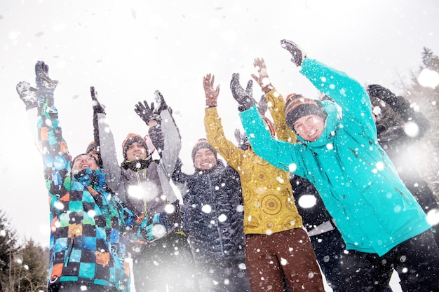 Gruppe junger glücklicher Geschäftsleute, die Spaß daran haben, Schnee in die Luft zu werfen, während sie während eines Teambuildings im Bergwald einen verschneiten Wintertag mit Schneeflocken um sich herum genießen