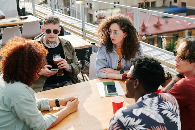 Gruppe junger interkultureller Freunde in Freizeitkleidung, die sich im Café im Freien ausruhen