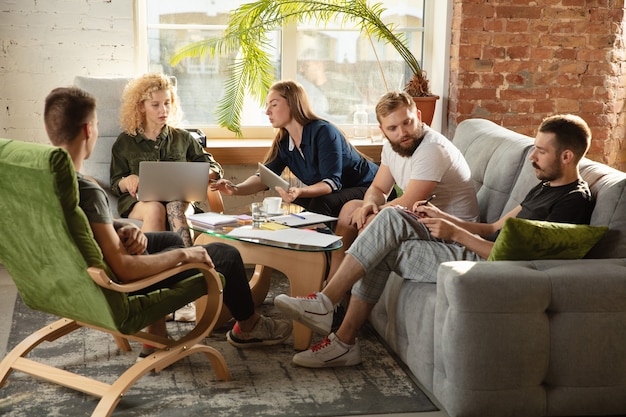 Gruppe junger kaukasischer Büroangestellter, die sich treffen, um neue Ideen zu diskutieren. Kreatives Treffen. Teamwork und Brainstorming. Männer und Frauen treffen sich im Büro, um ihre zukünftige Arbeit zu planen. Geschäftskonzept.