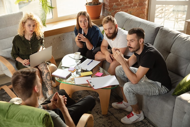 Gruppe junger kaukasischer Büroangestellter, die sich treffen, um neue Ideen zu diskutieren. Kreatives Treffen. Teamwork und Brainstorming. Männer und Frauen treffen sich im Büro, um ihre zukünftige Arbeit zu planen. Geschäftskonzept.