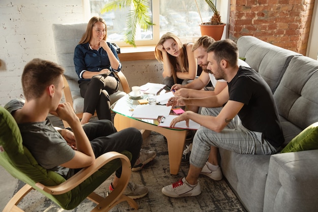 Gruppe junger kaukasischer Büroangestellter, die sich treffen, um neue Ideen zu diskutieren. Kreatives Treffen. Teamwork und Brainstorming. Männer und Frauen treffen sich im Büro, um ihre zukünftige Arbeit zu planen. Geschäftskonzept.