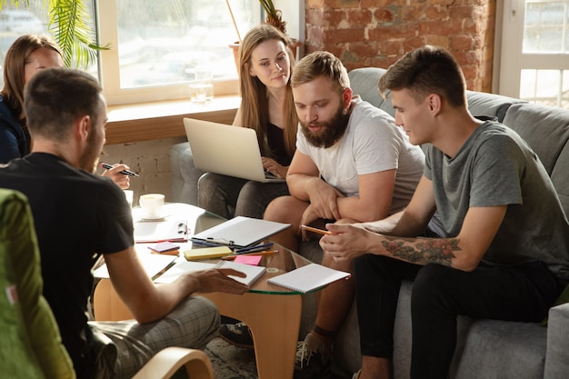 Gruppe junger kaukasischer Büroangestellter, die sich treffen, um neue Ideen zu diskutieren. Kreatives Treffen. Teamwork und Brainstorming. Männer und Frauen treffen sich im Büro, um ihre zukünftige Arbeit zu planen. Geschäftskonzept.