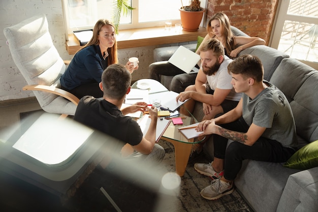 Gruppe junger kaukasischer Büroangestellter, die sich treffen, um neue Ideen zu diskutieren. Kreatives Treffen. Teamwork und Brainstorming. Männer und Frauen treffen sich im Büro, um ihre zukünftige Arbeit zu planen. Geschäftskonzept.