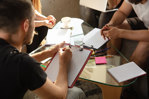 Gruppe junger kaukasischer Büroangestellter, die sich treffen, um neue Ideen zu diskutieren. Kreatives Treffen. Teamwork und Brainstorming. Männer und Frauen treffen sich im Büro, um ihre zukünftige Arbeit zu planen. Unternehmenskonzept.