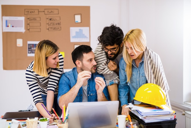 Gruppe junger kreativer Designer, die über einem Tisch stehen und über Probleme bei ihrer Arbeit sprechen.