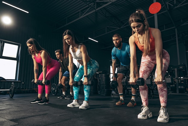 Gruppe junger Leute, die drinnen im Fitnessstudio trainieren Beibehaltung des sportlichen Lebensstils