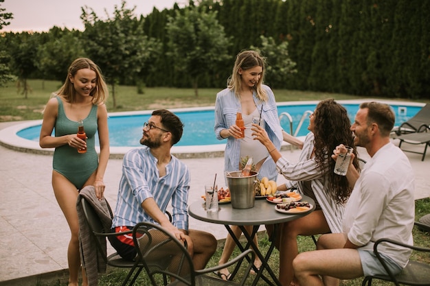 Gruppe junger Leute, die mit Apfelwein am Pool im Garten jubeln