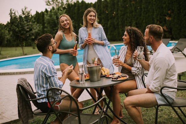 Gruppe junger Leute, die mit Apfelwein am Pool im Garten jubeln