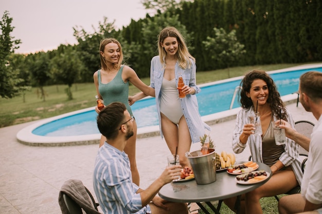 Gruppe junger Leute, die mit Apfelwein am Pool im Garten jubeln