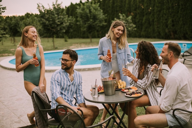 Gruppe junger Leute, die mit Apfelwein am Pool im Garten jubeln