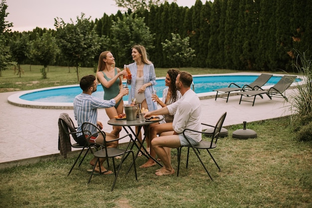 Gruppe junger Leute, die mit Apfelwein am Pool im Garten jubeln