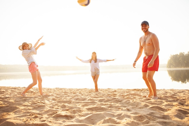 Gruppe junger Leute, die mit Ball am Strand spielen. Junge Freunde genießen Sommerferien an einem Sandstrand.