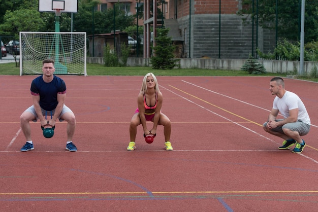 Foto gruppe junger leute, die mit einem lehrer eine kettle bell-übung im freien machen