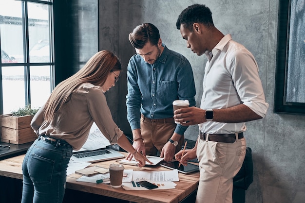 Gruppe junger Leute in eleganter Freizeitkleidung, die während der Arbeit im Büro über Geschäfte diskutieren