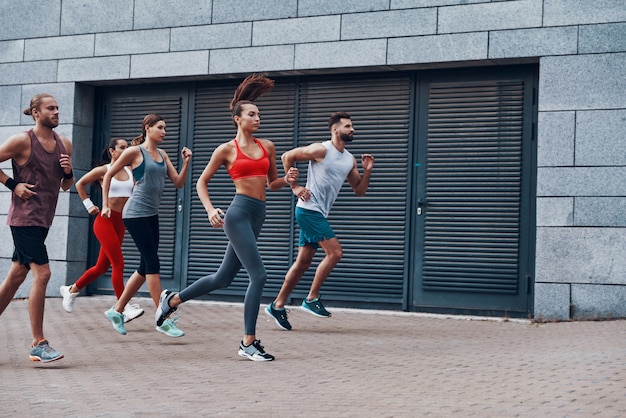 Gruppe junger Leute in Sportkleidung, die beim Training auf dem Bürgersteig im Freien joggen