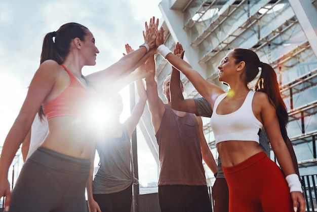 Gruppe junger Leute in Sportkleidung, die sich gegenseitig High Five geben und lächeln, während sie im Freien trainieren