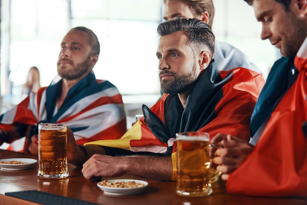 Gruppe junger Männer, die mit internationalen Flaggen bedeckt sind und Bier genießen?