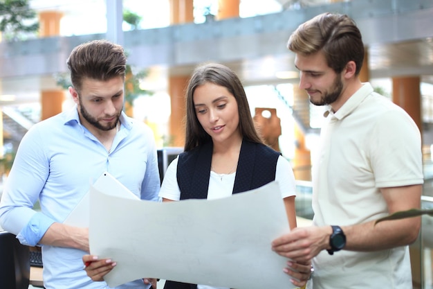 Gruppe junger moderner Menschen in intelligenter Freizeitkleidung, die ein Brainstorming-Meeting beim Stehen im Kreativbüro haben.