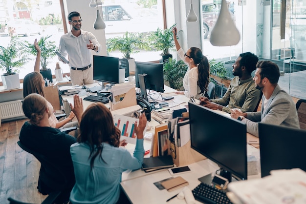 Gruppe junger moderner Menschen in intelligenter Freizeitkleidung, die während der Arbeit im Büro kommunizieren und moderne Technologien verwenden