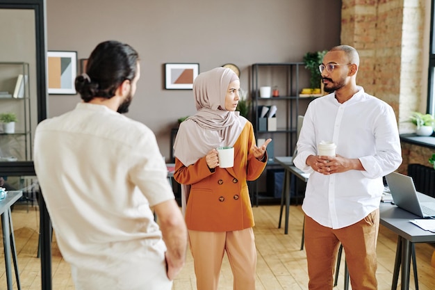 Gruppe junger muslimischer Mitarbeiter, die Kaffee trinken und Pläne diskutieren