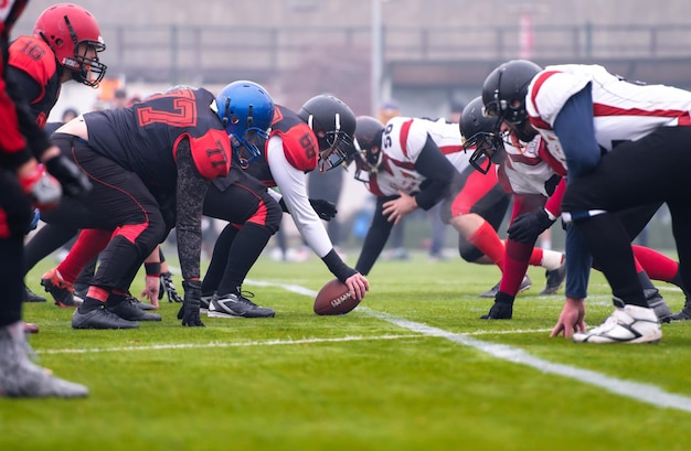 Gruppe junger professioneller American-Football-Spieler, die während des Trainingsspiels auf dem Stadionfeld startbereit sind