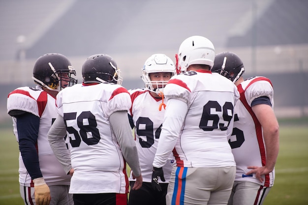 Gruppe junger professioneller American-Football-Spieler, die zur Halbzeit während des Trainingsspiels auf dem Stadionfeld gemeinsam über Strategie diskutieren