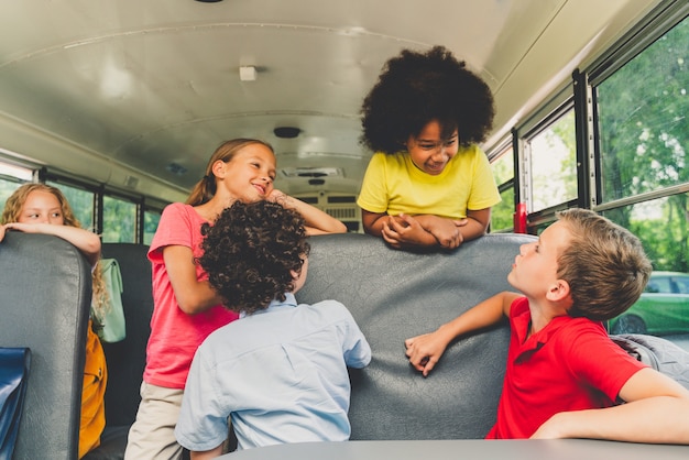 Gruppe junger Schüler, die die Grundschule in einem gelben Schulbus besuchen - Grundschulkinder, die Spaß haben