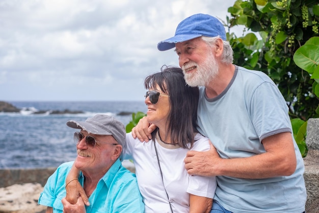 Gruppe lächelnder älterer kaukasischer Freunde, die am Meer sitzen und den Tag im Freien genießen und wegsehen Senioren genießen den Ruhestand und die Freizeit