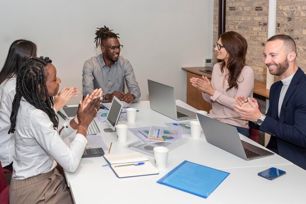 Gruppe lächelnder multiethnischer Geschäftsleute, die zusammenarbeiten und dem Teamleiter im Büro applaudieren
