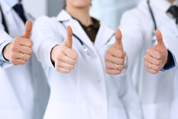 Gruppe moderner Ärzte, die als Team mit Daumen nach oben im Krankenhausbüro stehen