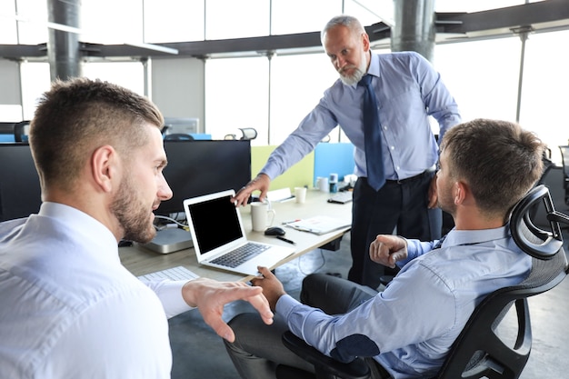 Gruppe moderner Geschäftsleute in formeller Kleidung, die Börsendaten analysiert, während sie im Büro arbeiten.