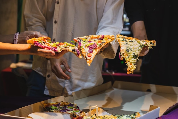 Gruppe nicht erkennbarer Menschenhände, die ein Stück Pizza halten