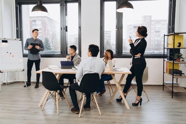 Gruppe positiver multikultureller Marketingexperten, die den Arbeitsprozess planen und Ideen austauschen, während sie eine Werbekampagne erstellen. Junge Kollegen, die im Loft-Innenbüro zusammenarbeiten