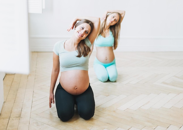Foto gruppe schwangerer frauen in sportuniformen, die im hellen studio turnen
