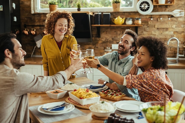 Gruppe sorgloser Freunde, die mit Weingläsern anstoßen, während sie zu Hause zu Mittag essen.