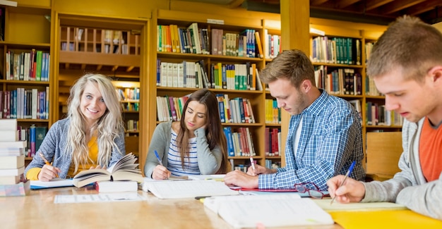 Gruppe Studenten, die Anmerkungen am Bibliotheksschreibtisch schreiben